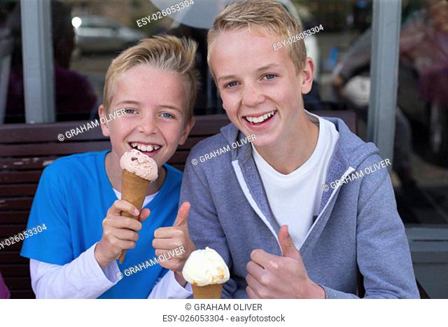 Brothers enjoying ice cream outside of a shop. They are wearing casual clothing and smiling at the camera