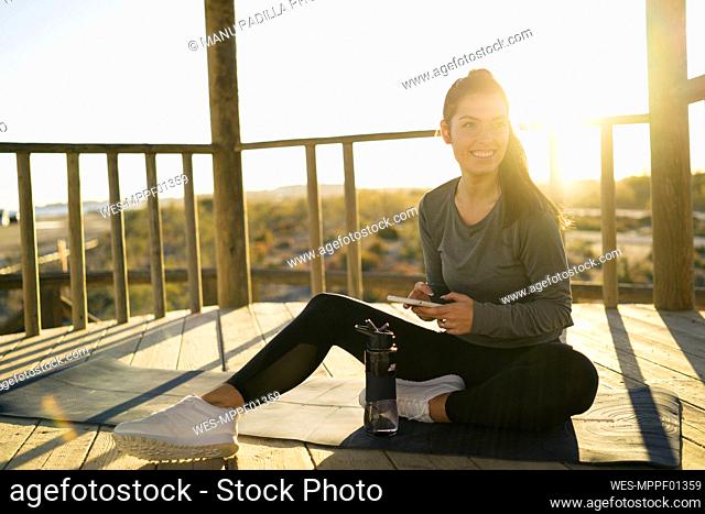 Smiling young woman using smart phone while sitting on mat in gazebo