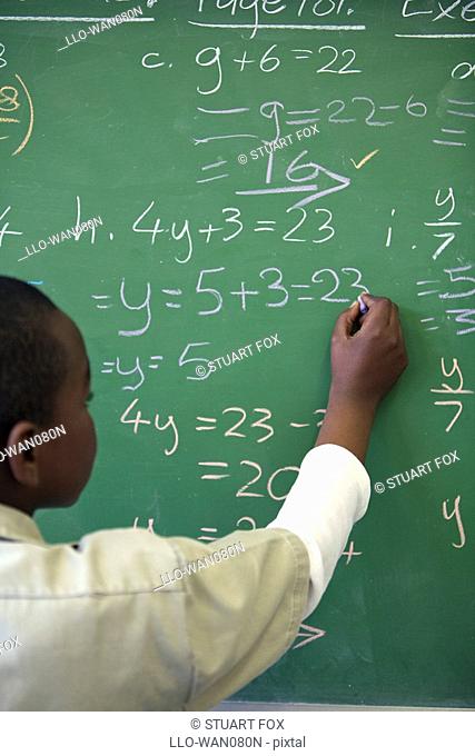 Schoolboy writing algebra sums on the classroom chalkboard, KwaZulu Natal Province, South Africa