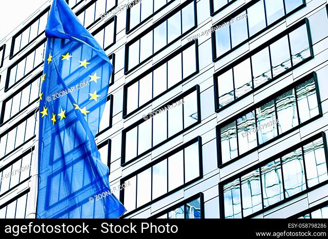 European Union flag waving in front of modern corporate office building, symbol of EU Parliament, Commission and Council