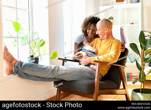 Happy family with sleeping baby sitting on armchair at home