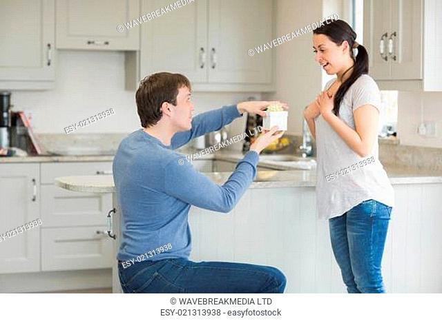 Woman getting a present from husband on one knee in kitchen