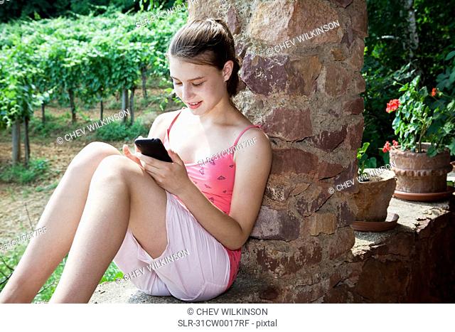 Girl using smartphone sitting on wall