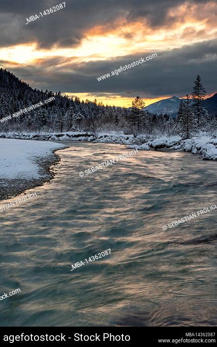 Dense clouds during sunset in the Isar meadows near Wallgau in the Karwendel, with the creek bed / river course in the foreground