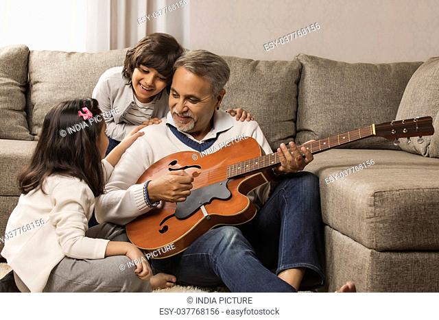 Grandfather playing guitar for grandchildren at home