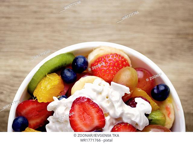 Sweet tasty fruit salad in the bowl with whipped cream