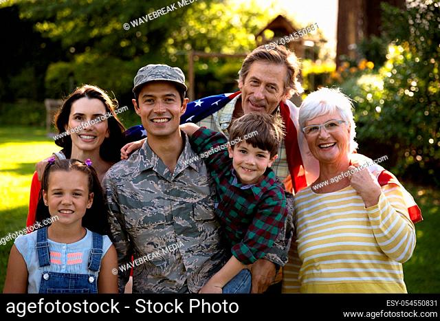 Portrait of a young adult mixed race male soldier and his diverse multi-generation family in the garden outside their home, embracing and smiling to camera