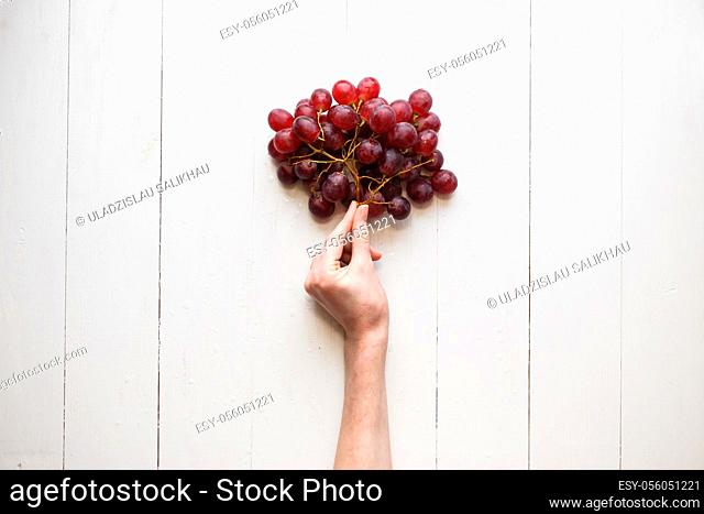 The girl's hand holds on to a bunch of red grapes on a wooden background. View from above. Grapes are like balloons