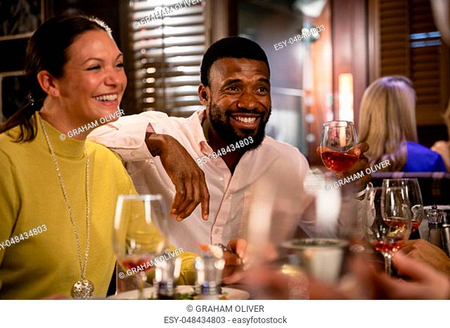 Mid adult couple sitting in a restaurant, enjoying a meal and drinks. They are smiling and laughing