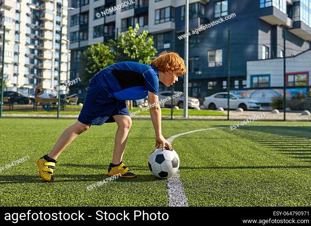 Concentrated schoolboy child putting ball on strip line on football field. Start soccer game match concept