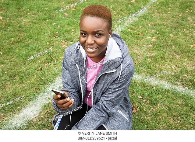 Black woman sitting on field listening to cell phone