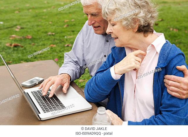 Husband and wife learning to use laptop in the park