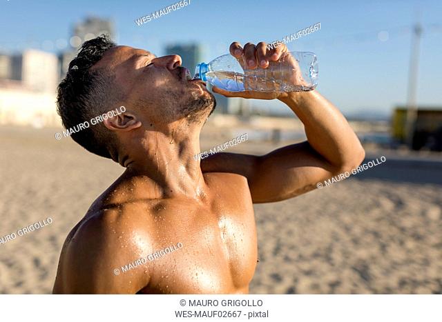 Barechested man drinking water after workout on the beach