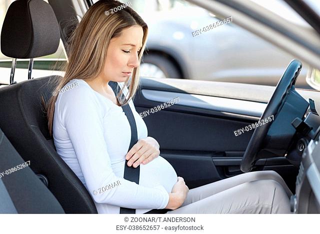 Young pregnant woman behind the steering wheel having contractions