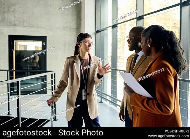 Businesswoman discussing with coworkers by glass window in convention center