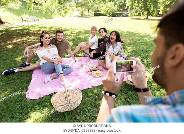 man photographing friends by smartphone at picnic