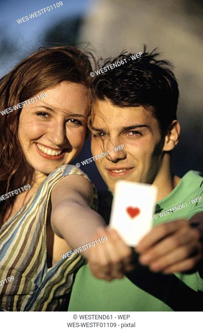 Young couple showing ace of hearts, focus on couple at background, close-up