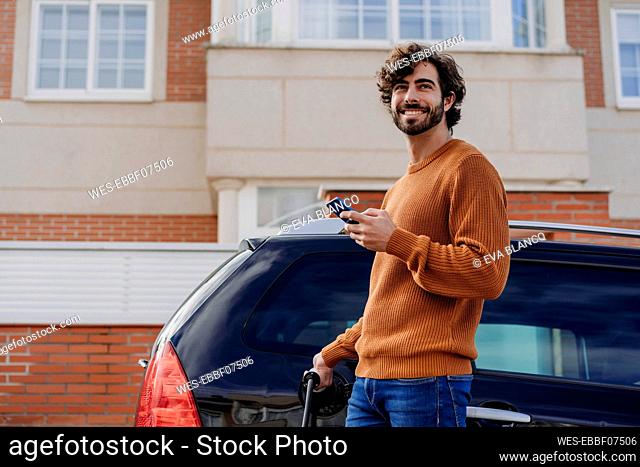 Happy young man charging car in front of building