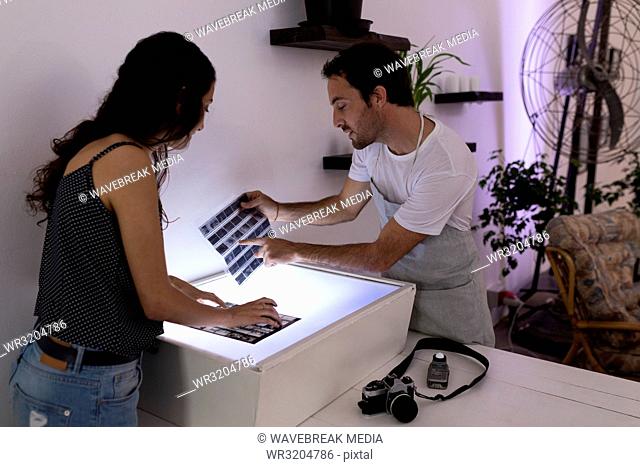 Male photographer and female model discussing over negative filmstrip