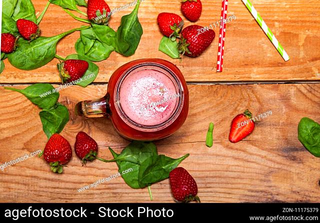 Strawberry smoothie or milkshake in a jar and spinach leaves on wooden background, healthy food for breakfast and snack
