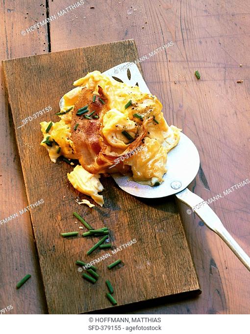 Scrambled egg with bacon and chives on wooden board