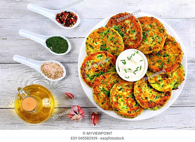 delicious zucchini fritters on white plate with sour cream in centre of dish sprinkled with finely chopped chives, spices