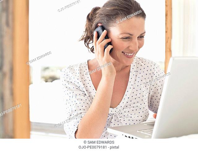 Woman using laptop and talking on cell phone