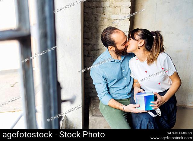 Couple with gift box kissing each other sitting by window