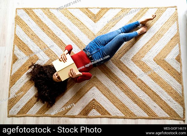 Woman with book lying on carpet at home