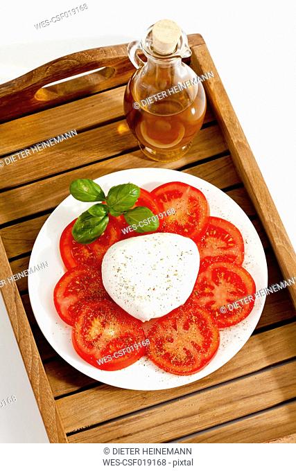 Buffalo mozzarella with basil, tomatoes and bottle of olive oil on plate, close up