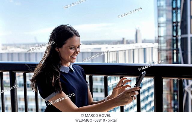 UK, London, smiling woman using cell phone on a roof terrace
