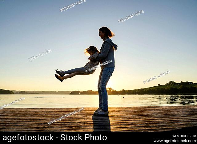Mother lifting and spinning girl on pier during weekend