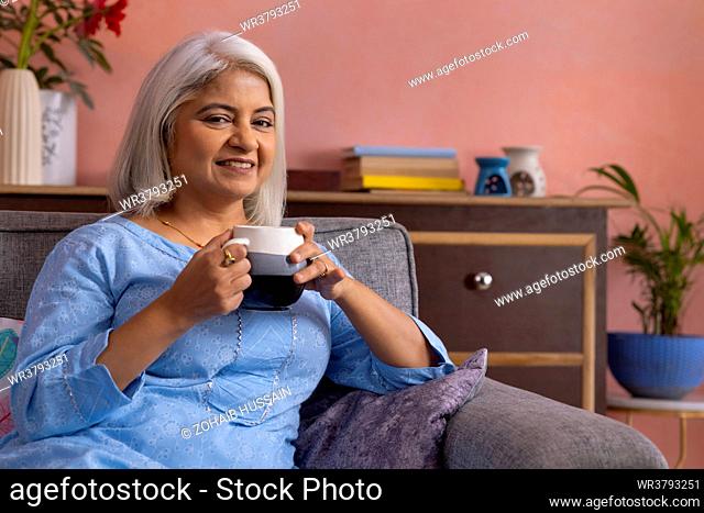 Old woman with holding a cup of tea in hand looking at camera