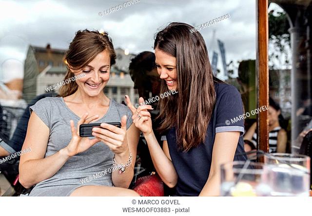Dos mujeres divirtiéndose con su smartphone en una terraza
