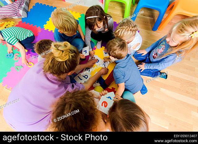 Group of kindergarten kids sitting closely on a floor together with teacher, providing group work. Children learning to cooperate while solving tasks