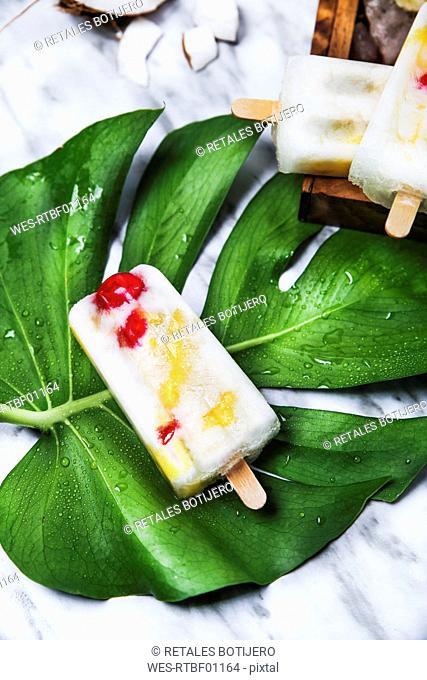 Pina Colada popsicle with candied cherries and pineapple on leaf