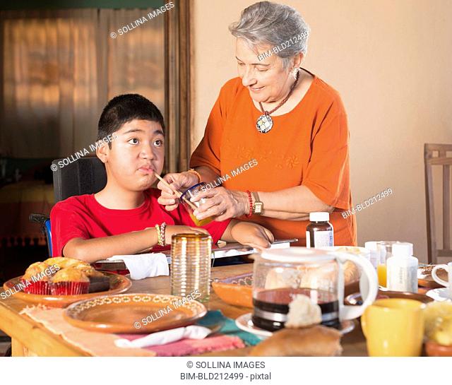 Hispanic woman helping grandson drink through straw