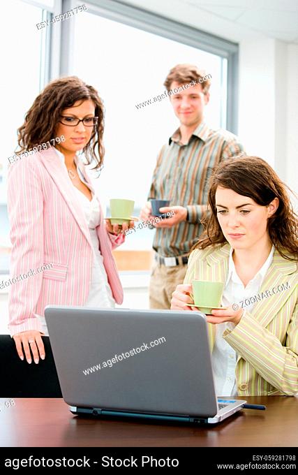 Team of young successful office workers talking and drinking coffee at meeting room, businesswoman working on laptop computer in front