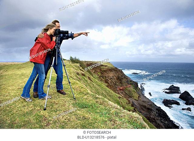 Couple looking off the coast through a camera on a tripod