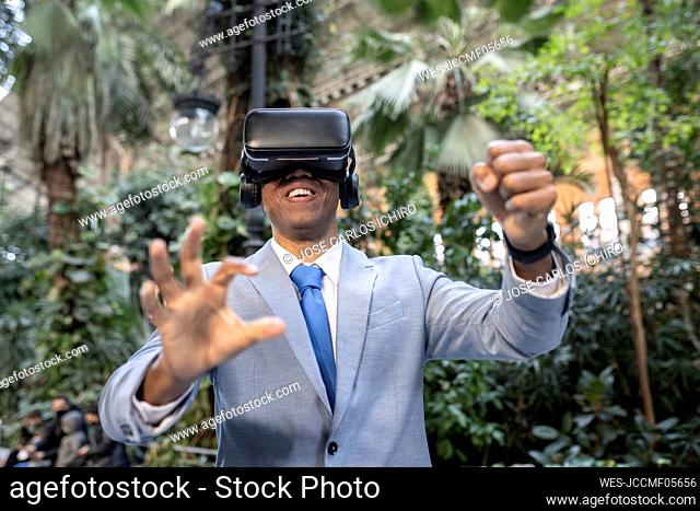 Smiling businessman wearing virtual reality simulator gesturing in front of plants