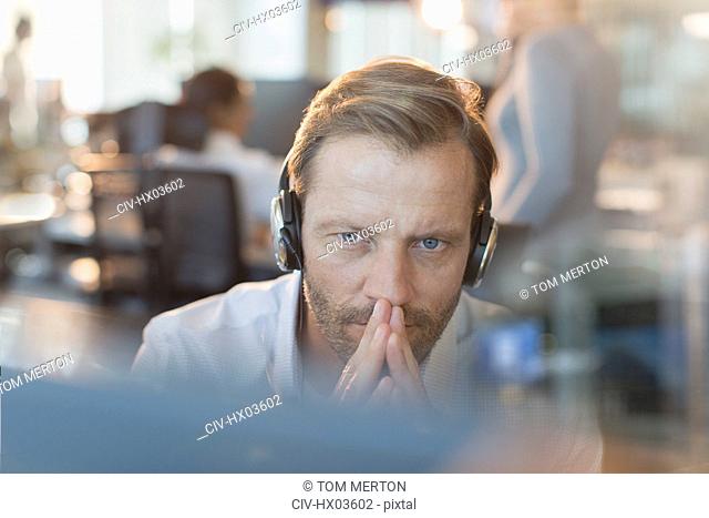 Serious businessman wearing headphones, working at computer