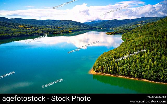 Summer landscape with lake and mountain woodland. Reflection of sky, clouds, forest and mountains in water. Aerial view of Reservoir/lake Starina