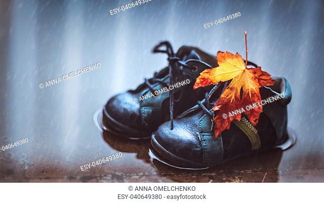 Closeup photo of a small baby boots in the puddle with dry maple leaf on it, waterproof child's shoes, autumn season concept