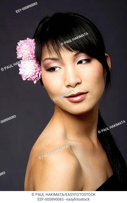 Beautiful face of an Asian-American woman with purple pink white flowers in her hair, looking to her side, isolated