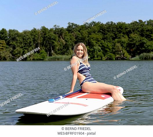 Germany, Brandenburg, portrait of smiling young woman relaxing on paddleboard on Zeuthener See