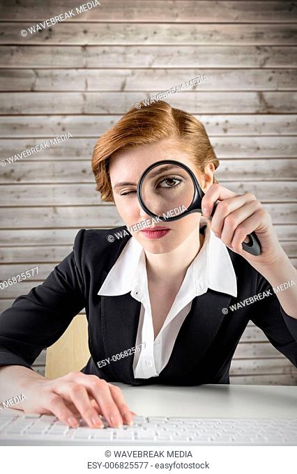 Composite image of redhead businesswoman looking through magnifying glass