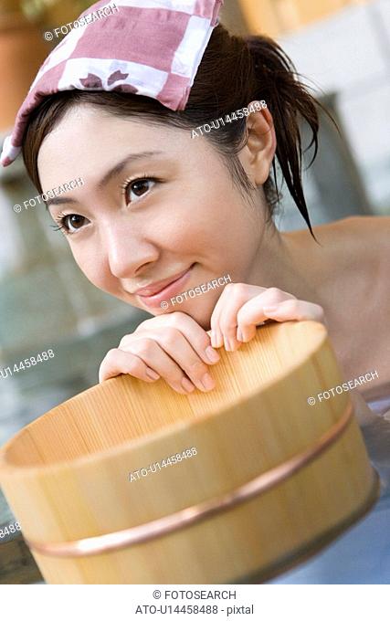 Woman in a hot tub holding a wooden pail, towel on her head, front view, Japan