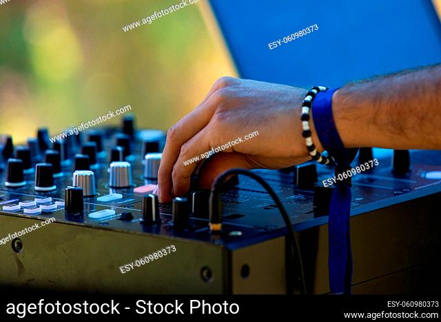 A close up view on the hand of an electronic music DJ turning dials on a CDJ mixer, wearing bangles against green blurry background at earth festival