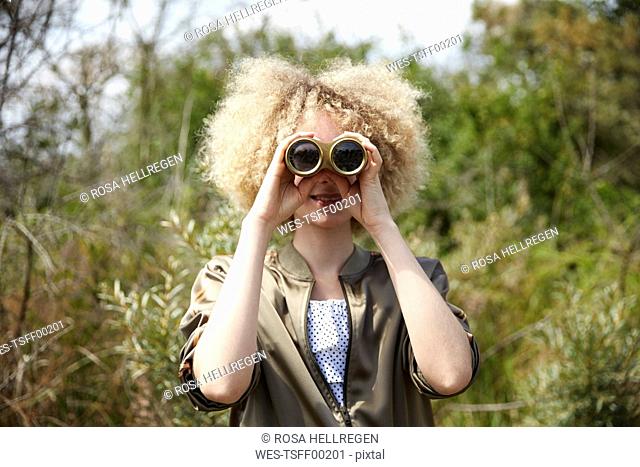 Young woman with curly hair looking through old binoculars