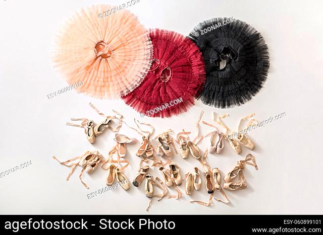 Three colorful tutus and many beige pointe shoes on the light floor in the studio. Tutus are peach, burgundy and black colored. Top view photo